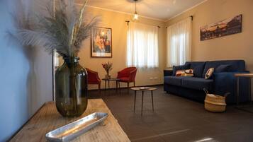 A living room with a sofa, chairs, a coffee table, a vase with dried plants, and a painting on the wall.