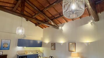 Ein Essbereich mit Holztisch und -stühlen, im Hintergrund eine Küche und eine Decke mit freiliegenden Balken.