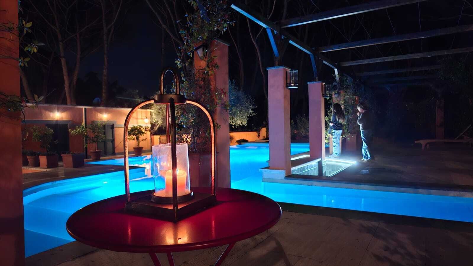 A pool area with a glass enclosure and a red table in the foreground, surrounded by pillars and potted plants.