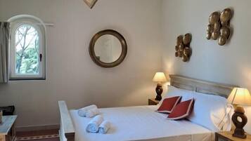 A hotel room with a wooden bed, a round mirror, two wall sconces, and a window with curtains.