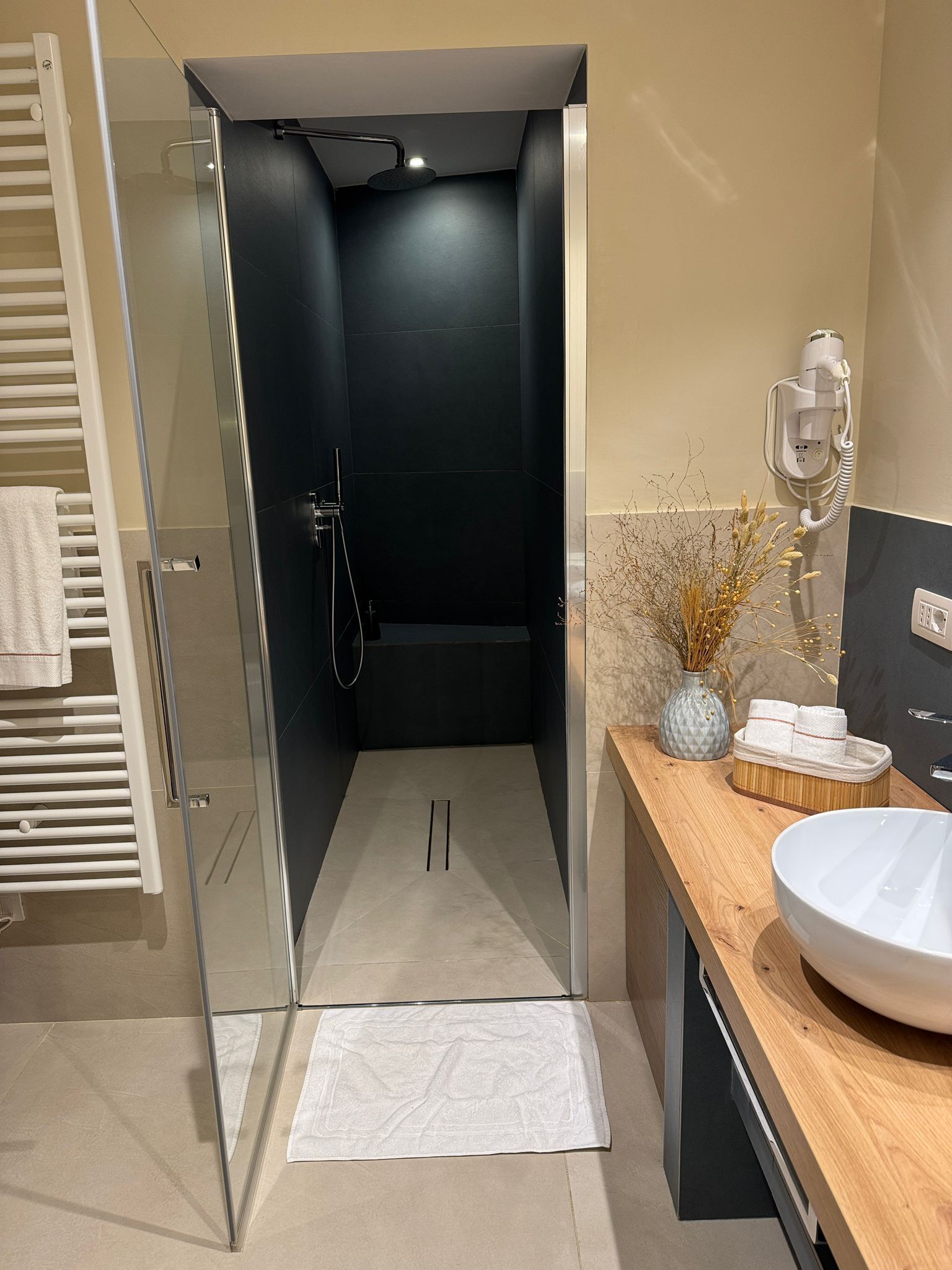 A modern bathroom with a glass-enclosed shower, a wooden vanity with a sink, and a towel rack.