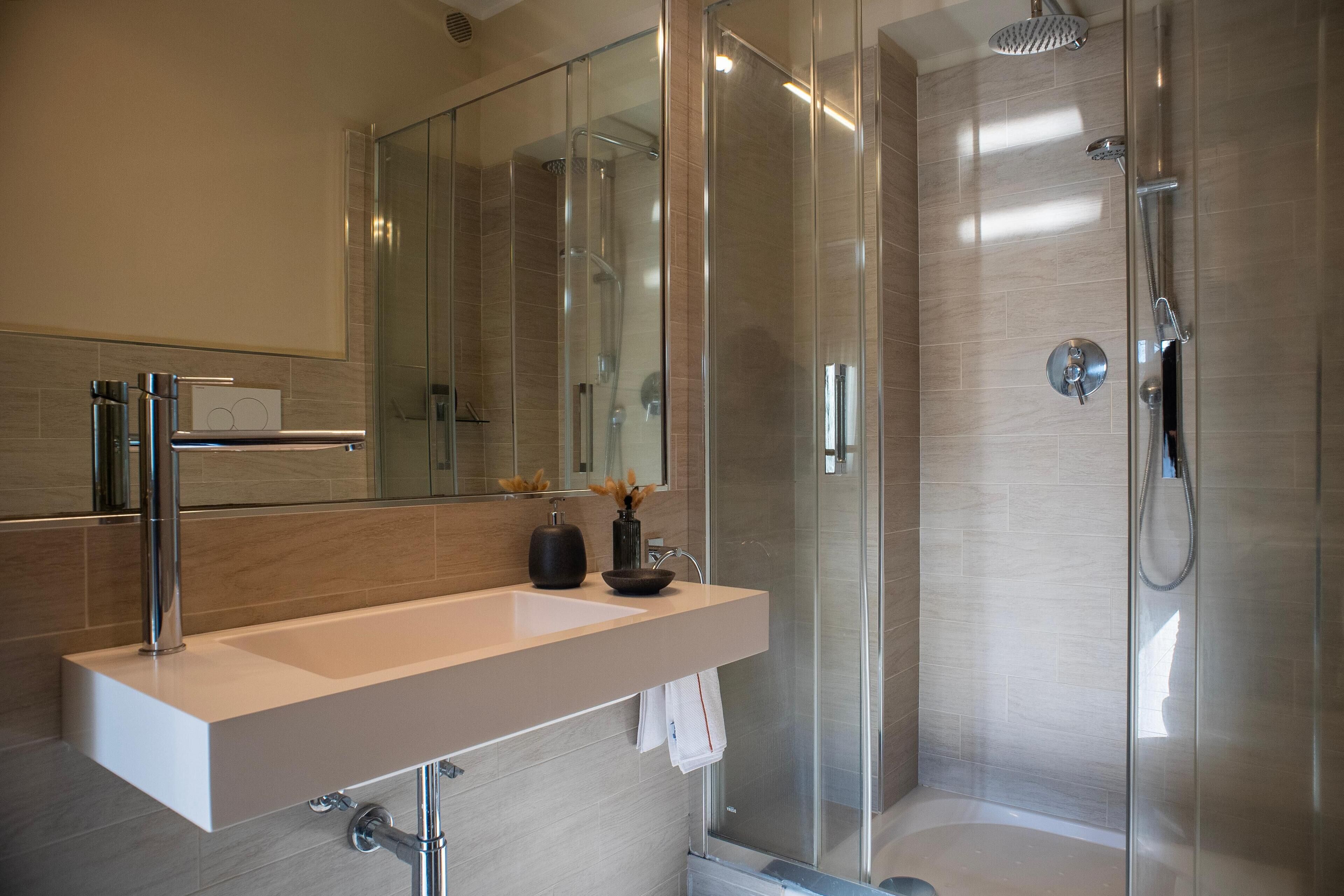 A modern bathroom with a glass-enclosed shower, a white sink, and a large mirror.