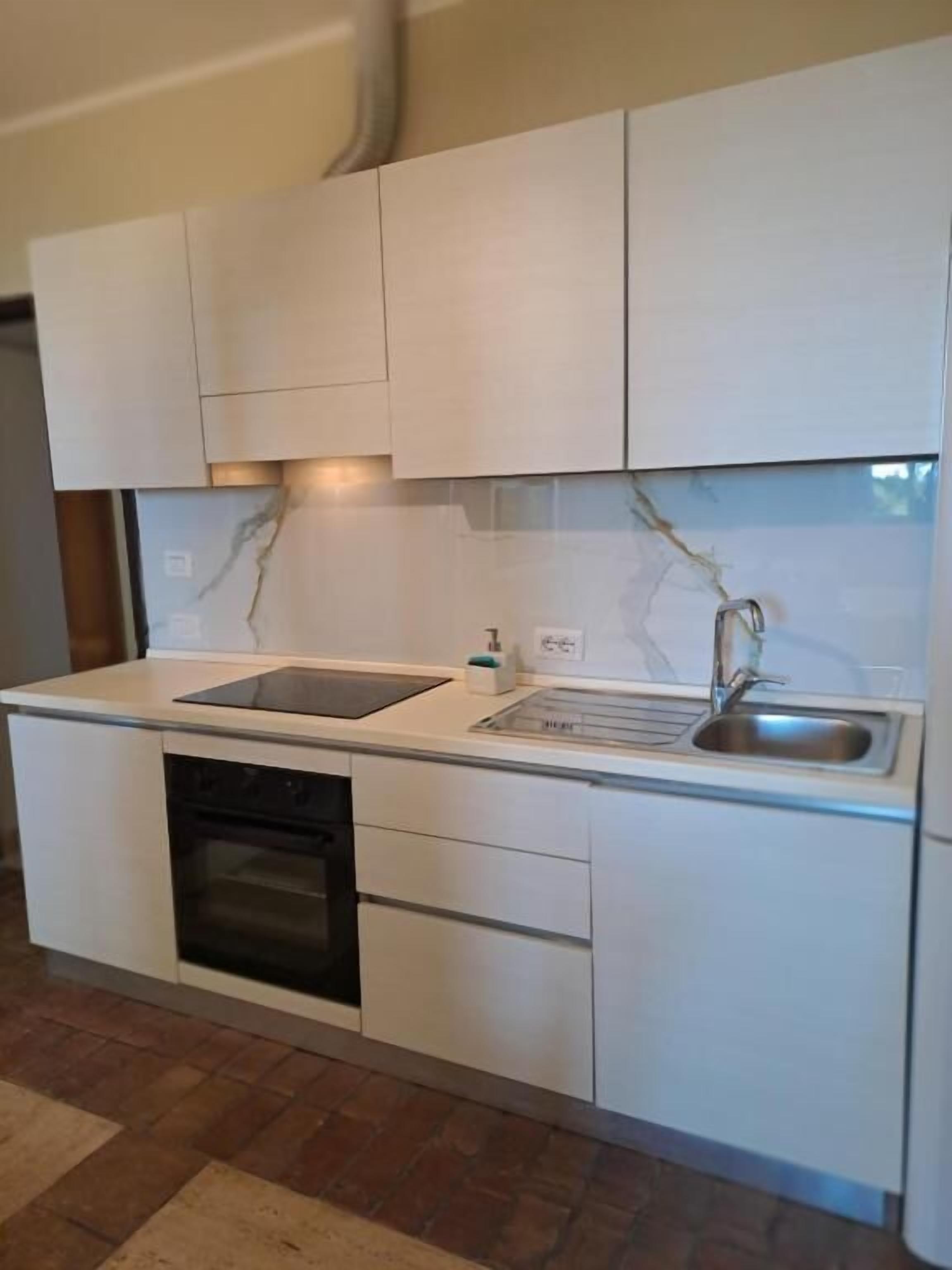 Eine kleine Küche mit weißen Schränken, einem Backofen, einer Spüle und einer Arbeitsplatte.