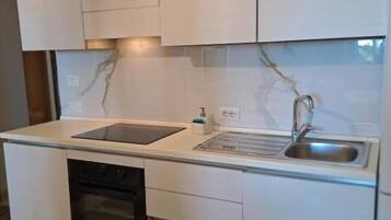 Eine kleine Küche mit weißen Schränken, einem Backofen, einer Spüle und einer Arbeitsplatte.