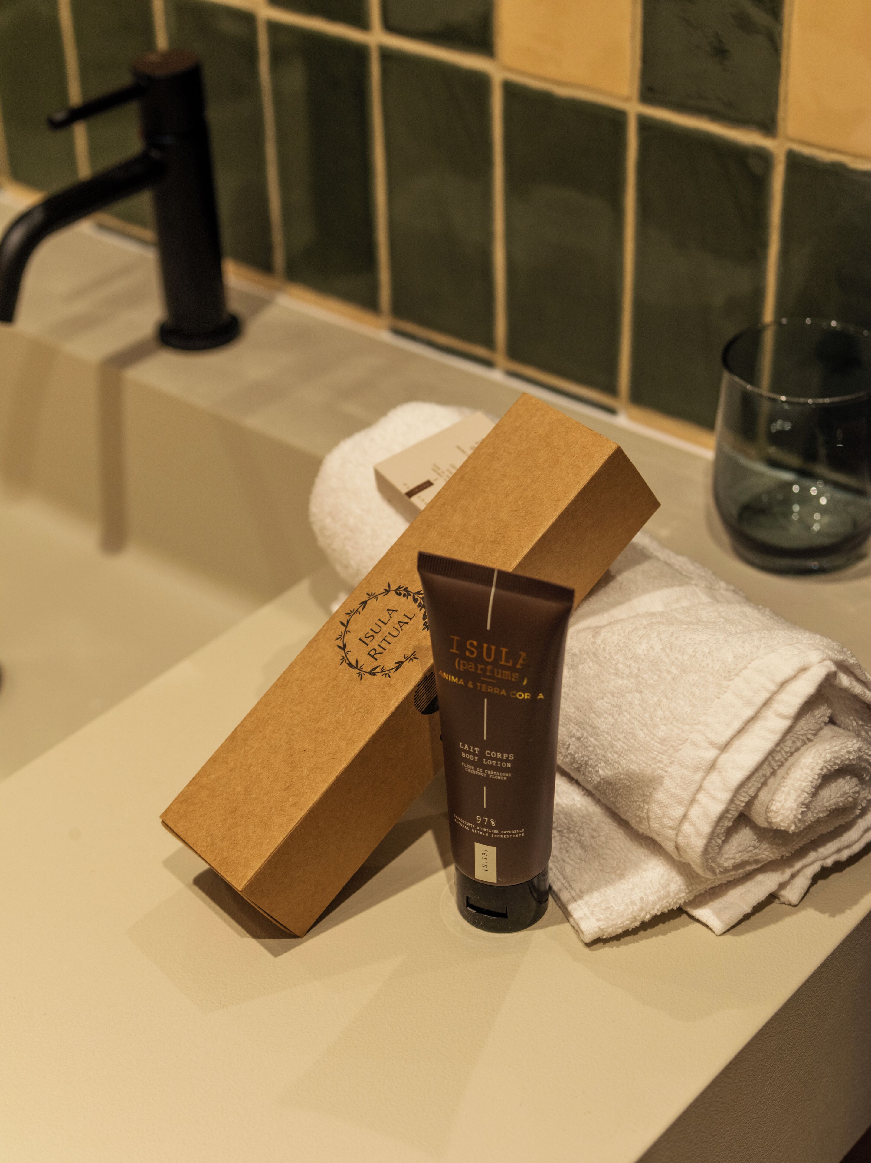 Baño con bañera, una toalla, una botella de loción corporal Isula Ritual y una caja marrón.