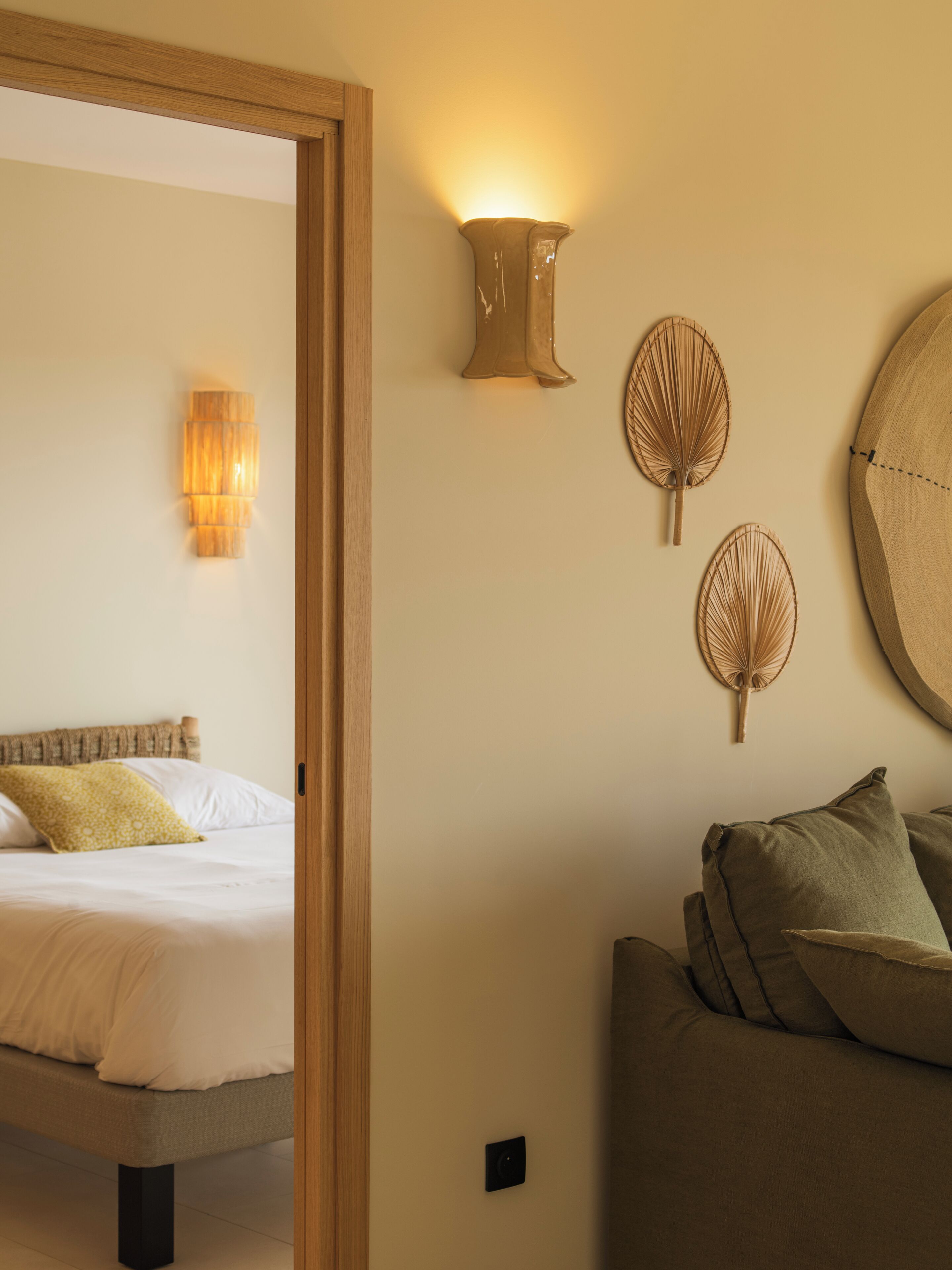 A hotel room with a bed, a sofa, a wall-mounted light, and decorative wall art.