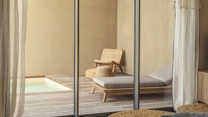 A modern room with a glass door leading to a balcony, a wicker chair, a cushioned bench, a woven stool, and a hanging light fixture. -  Résidence & Villas Oradoro (Belgodere)