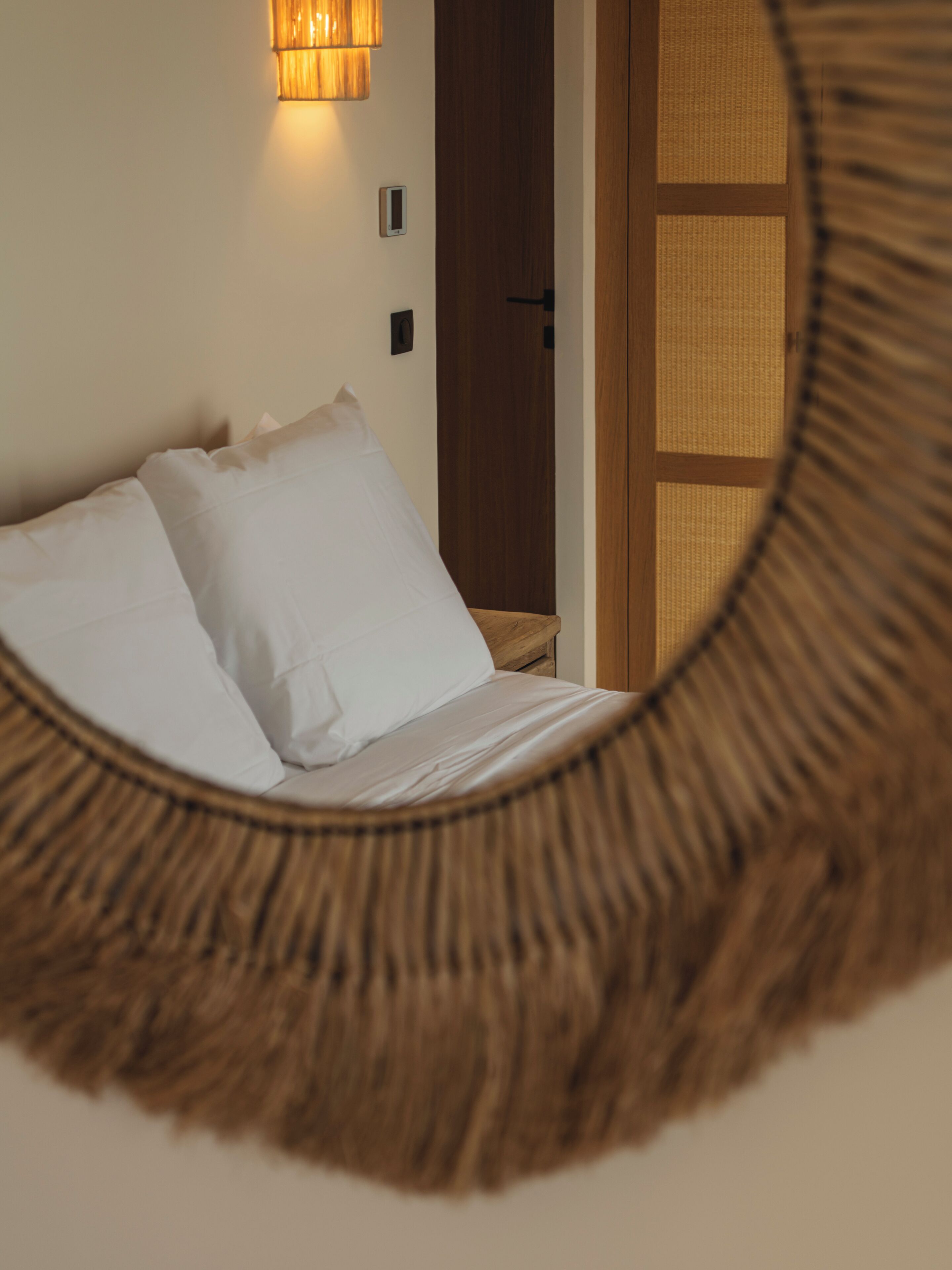 A bed with white linens, a wooden door, and a wall-mounted light fixture.