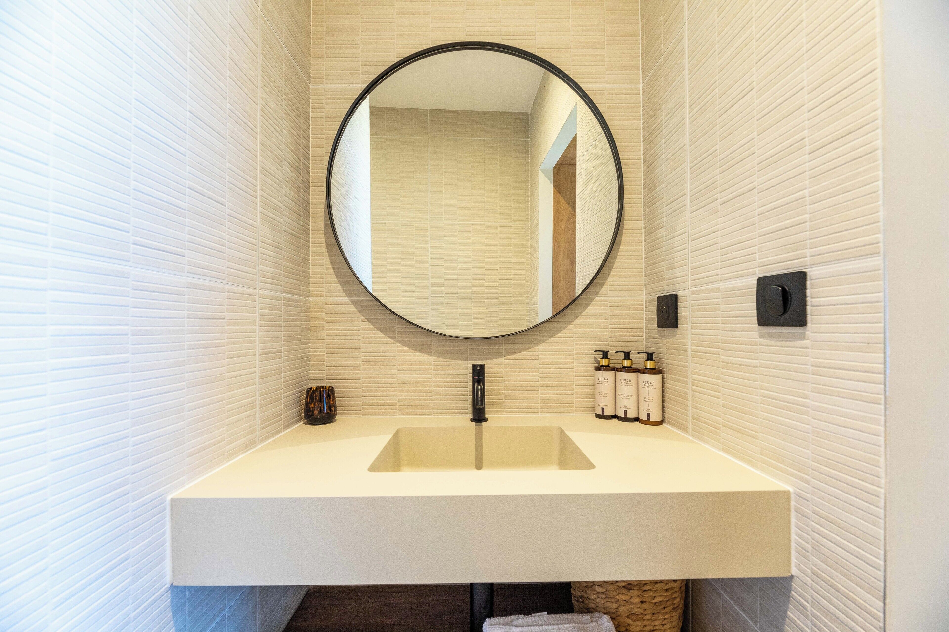 Une salle de bain avec un miroir rond, un lavabo et des articles de toilette fixés au mur.