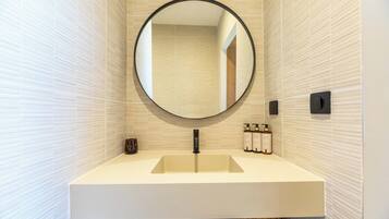 Une salle de bain avec un miroir rond, un lavabo et des articles de toilette fixés au mur.