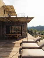Une terrasse en bois avec des chaises longues et un espace repas offrant une vue sur un paysage montagneux.