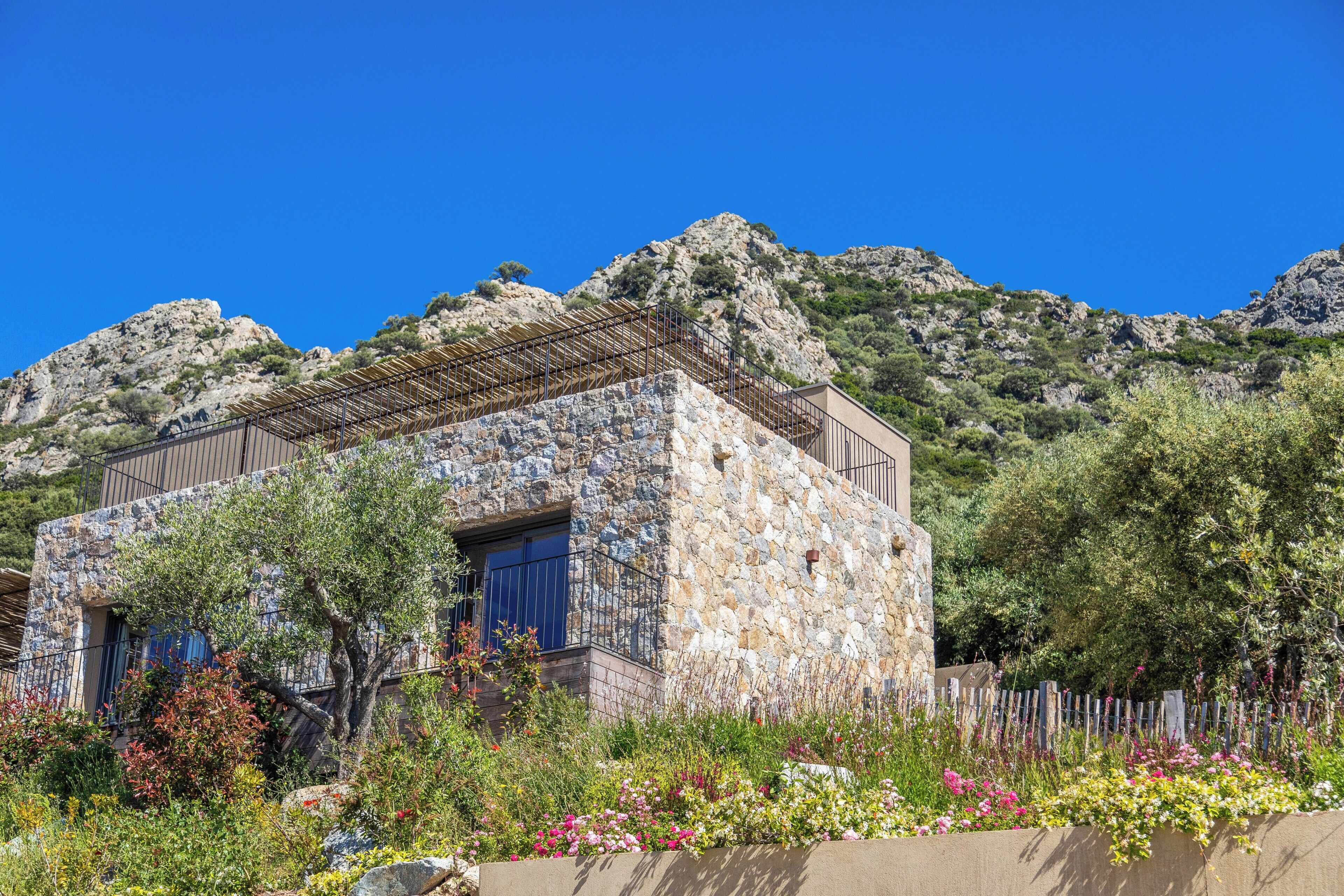 A stone building with a metal roof, surrounded by a variety of plants and flowers.