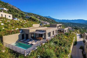 Une villa située sur une colline, dotée d’une piscine, d’un espace salon extérieur et offrant une vue sur les montagnes.