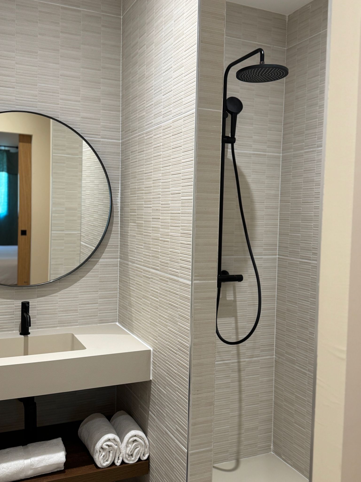 A modern bathroom with a white sink, a round mirror, and a black showerhead.