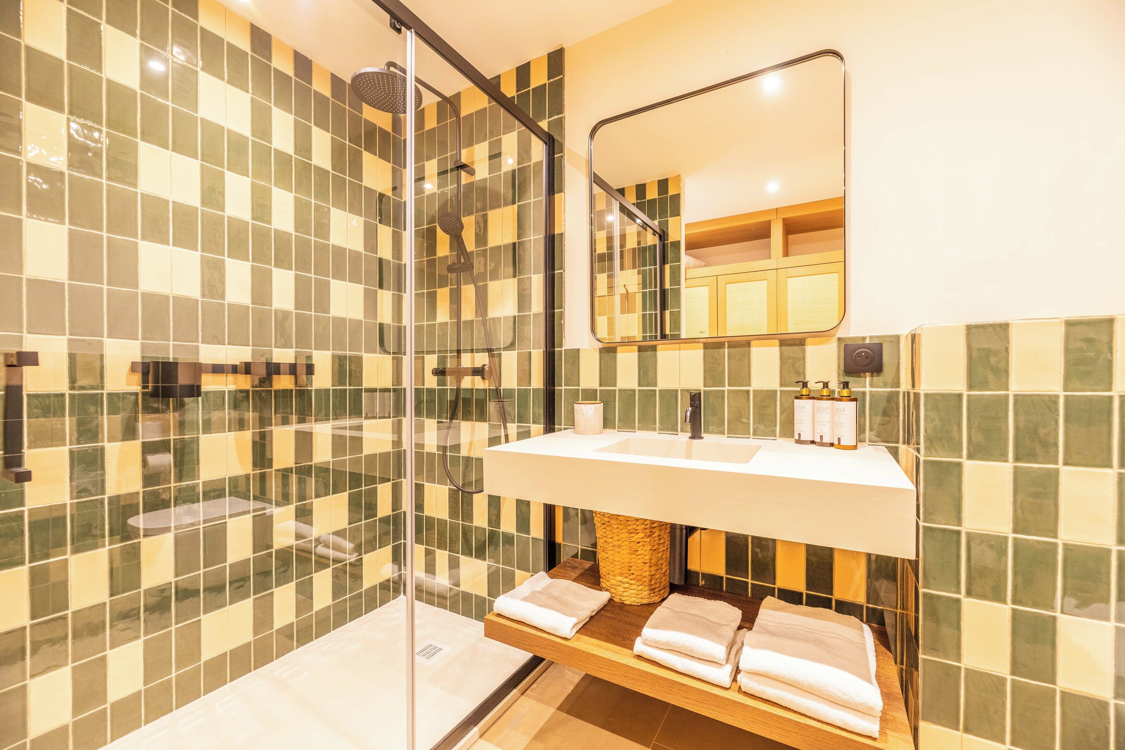 A modern bathroom with a glass-enclosed shower, a white sink with a mirror above, and a wooden shelf with towels.