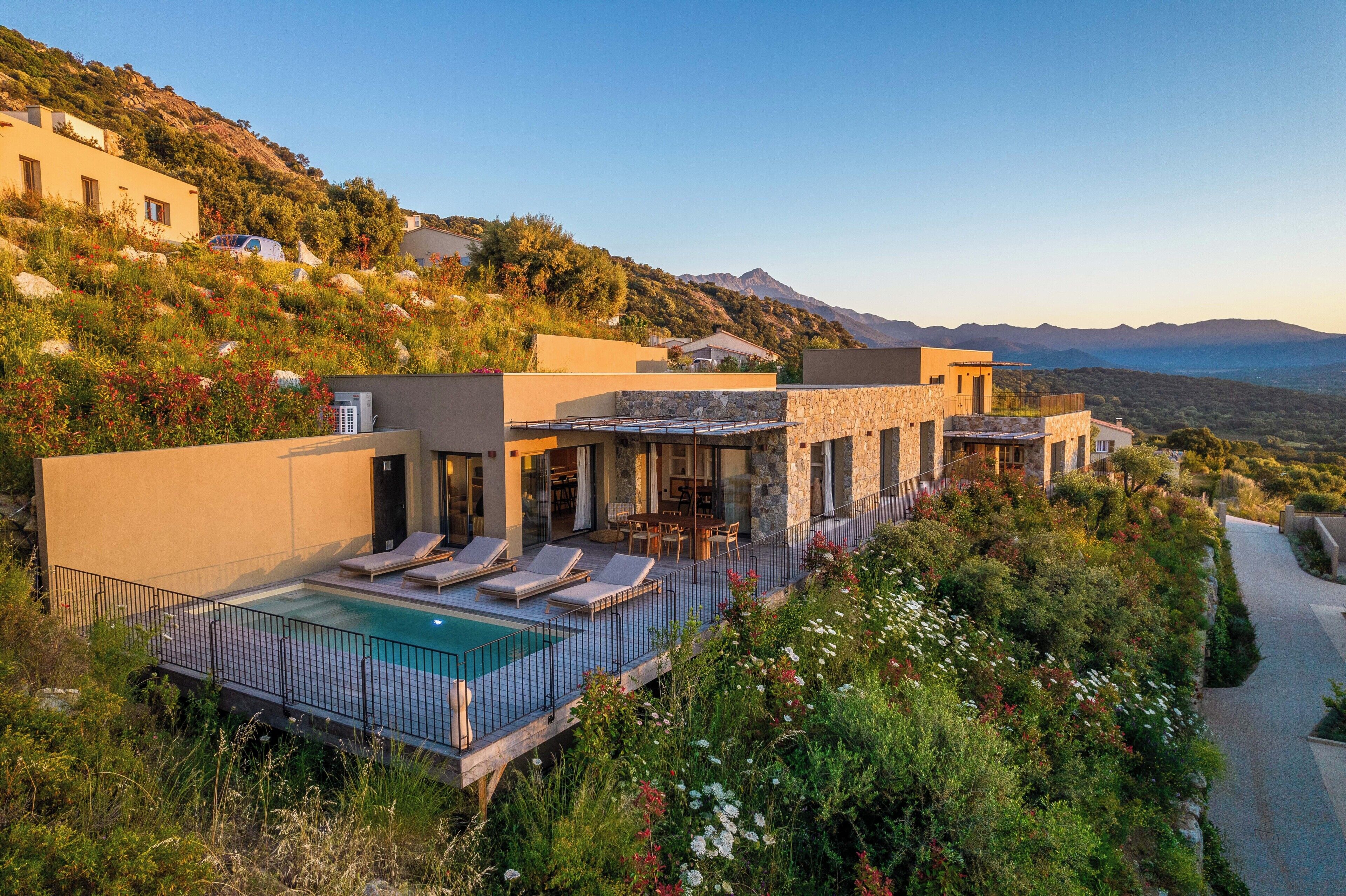 Una villa moderna con piscina, mobiliario exterior y vistas a la montaña.