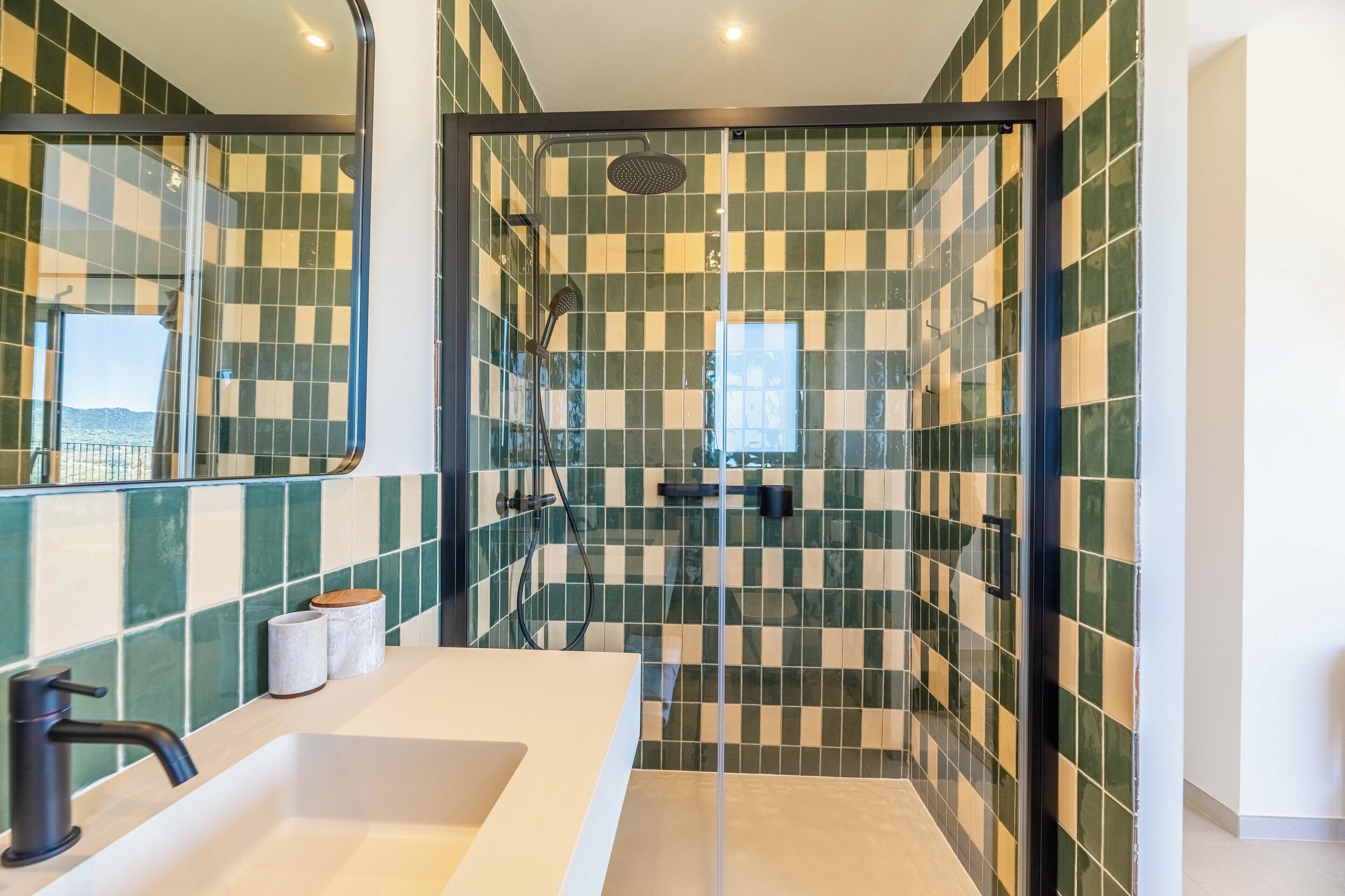 Un baño con pared de baldosas a cuadros, cabina de ducha de vidrio, lavamanos blanco y espejo.