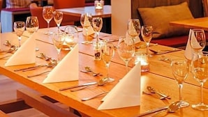 Restaurante com mesas de madeira preparadas para refeições, incluindo copos de vinho e talheres.
