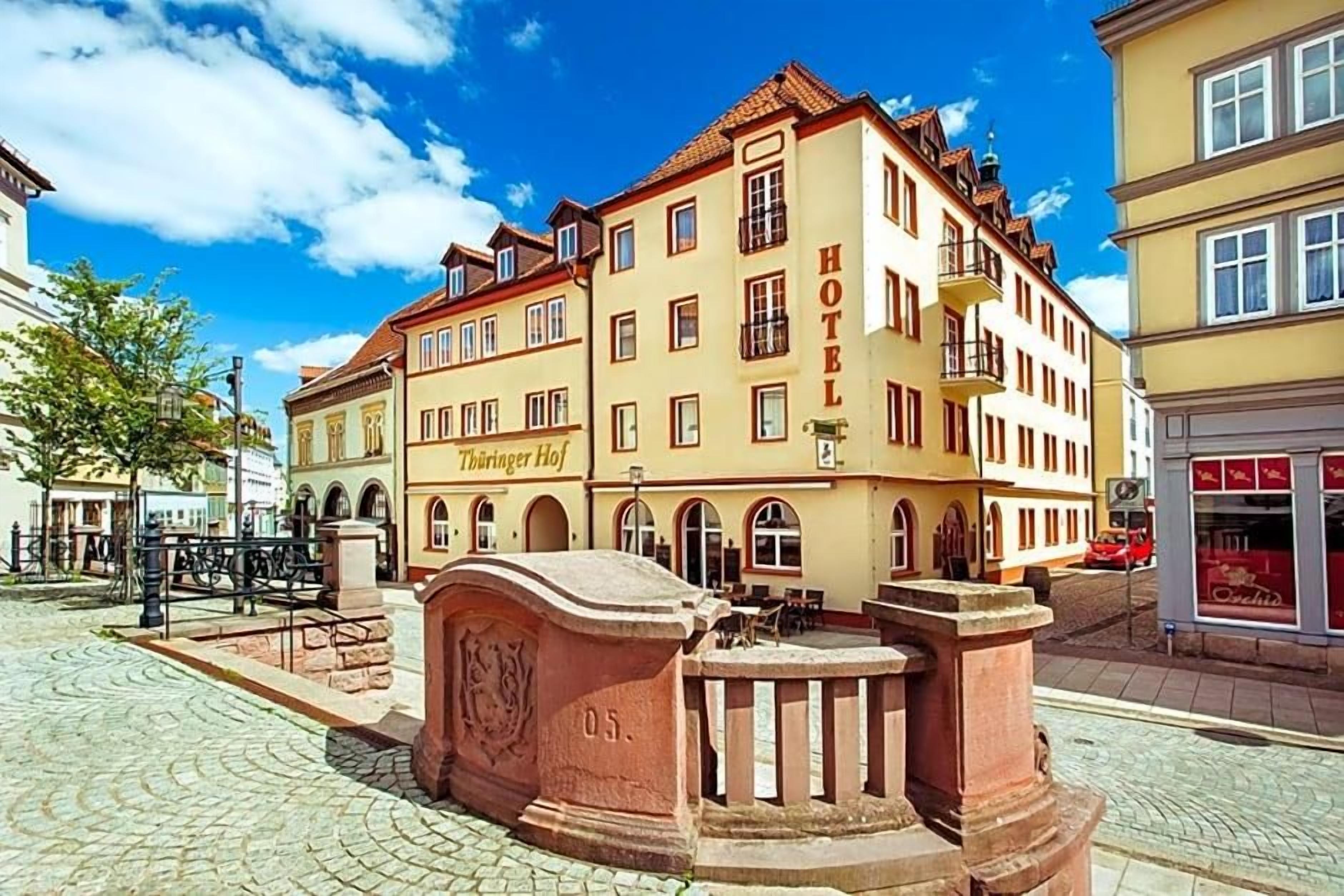 A historic building with a sign reading 'HOTEL Thüringer Hof.' It features a cobblestone courtyard, a fountain, and traditional architecture.