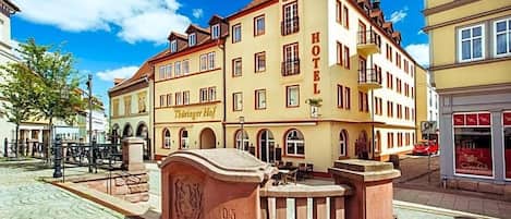 A historic building with a sign reading 'HOTEL Thüringer Hof.' It features a cobblestone courtyard, a fountain, and traditional architecture.