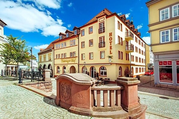 A historic building with a sign reading 'HOTEL Thüringer Hof.' It features a cobblestone courtyard, a fountain, and traditional architecture.