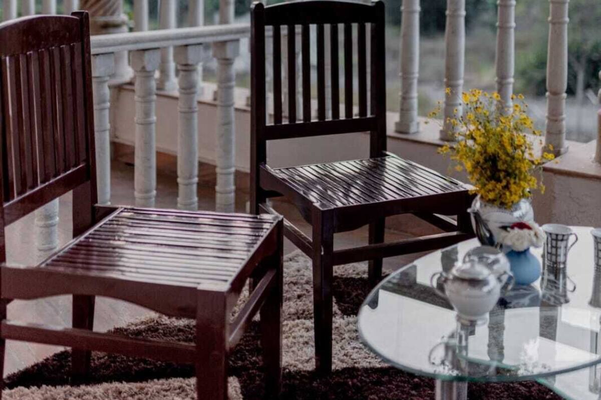 A balcony with two wooden chairs, a glass table, and a vase with yellow flowers.