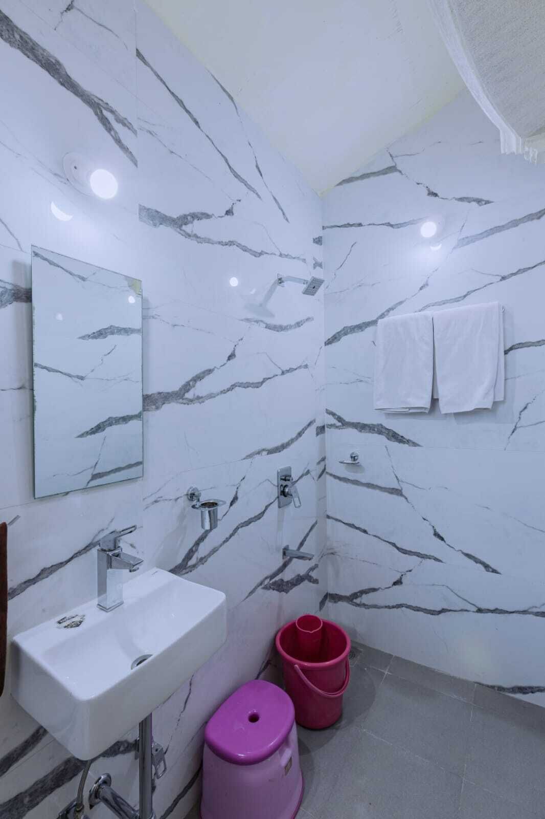 Une salle de bain avec un mur en marbre blanc, un lavabo, un miroir, une douche et des toilettes.