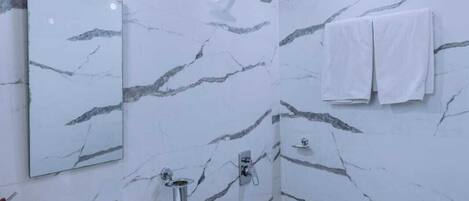 Une salle de bain avec un mur en marbre blanc, un lavabo, un miroir, une douche et des toilettes.