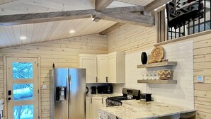 A modern kitchen with wooden walls, a stainless steel refrigerator, a coffee machine, and a marble island with bar stools. - Sundance Carriage House, Romantic, Sleeps 5 (Sundance)