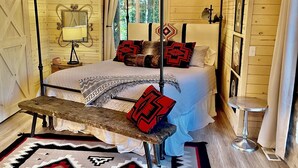 A wooden cabin bedroom with a four-poster bed, a bench, a lamp, and a window with curtains. - Sundance Carriage House, Romantic, Sleeps 5 (Sundance)