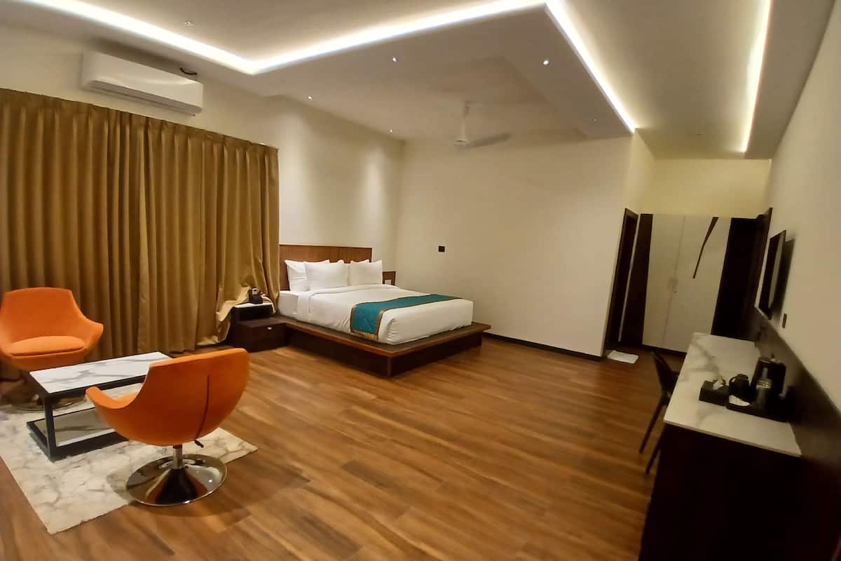 A modern hotel room with a bed, two orange chairs, a desk, and a TV.