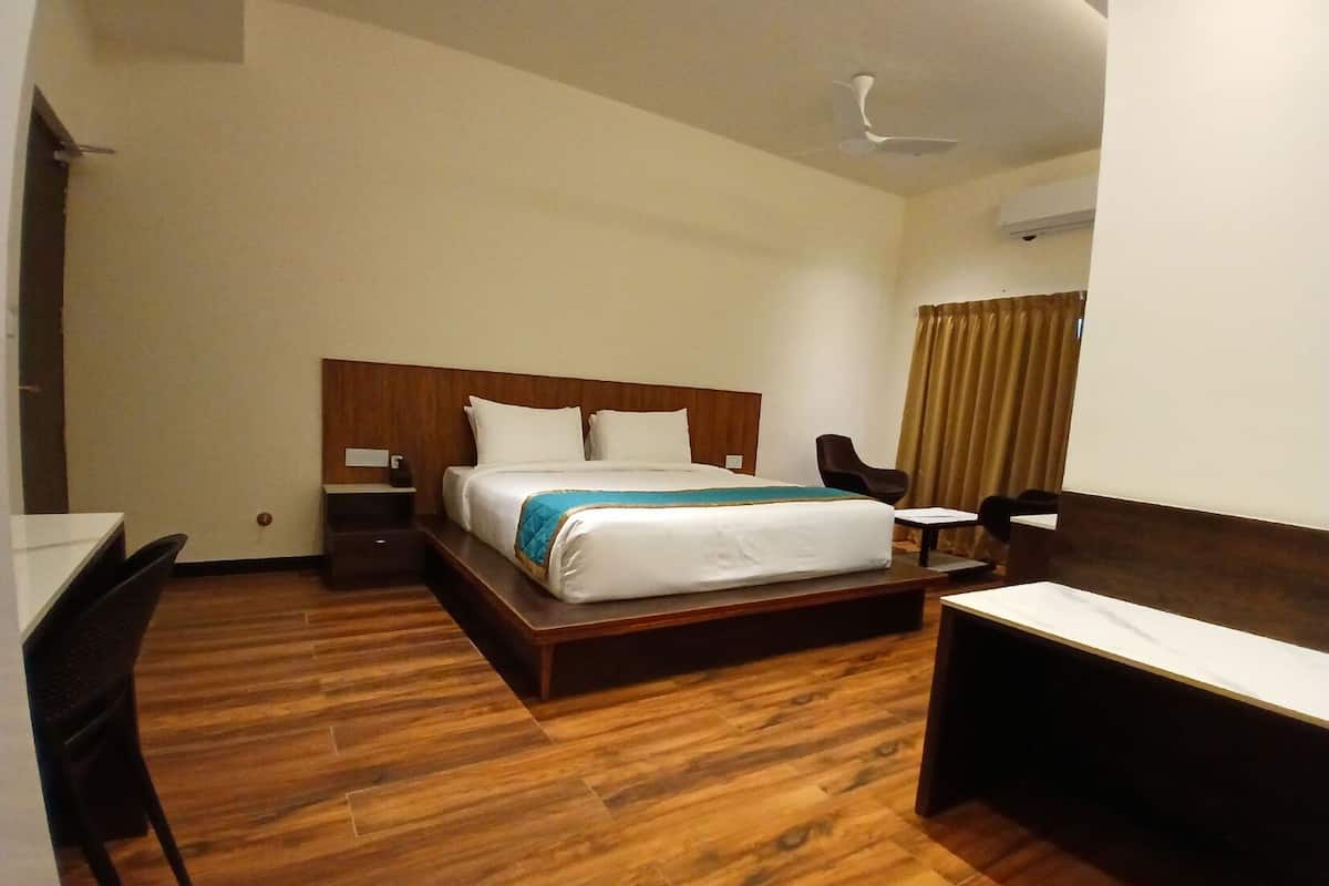 A hotel room with a wooden floor, a bed with white linens, a desk, a chair, and a small table.