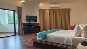 Ein modernes Hotelzimmer mit einem großen Bett, einem Flachbildfernseher, einem Schreibtisch und einer Glasschiebetür, die auf einen Balkon führt.