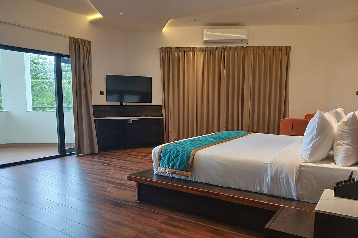 A modern hotel room with a large bed, a flat-screen TV, a desk, and a sliding glass door leading to a balcony.