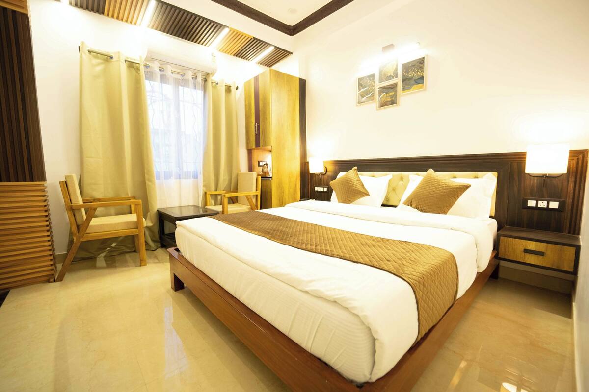 Quarto de hotel com uma cama grande, cabeceira de madeira, uma escrivaninha, uma cadeira e uma mesa de cabeceira com abajur.