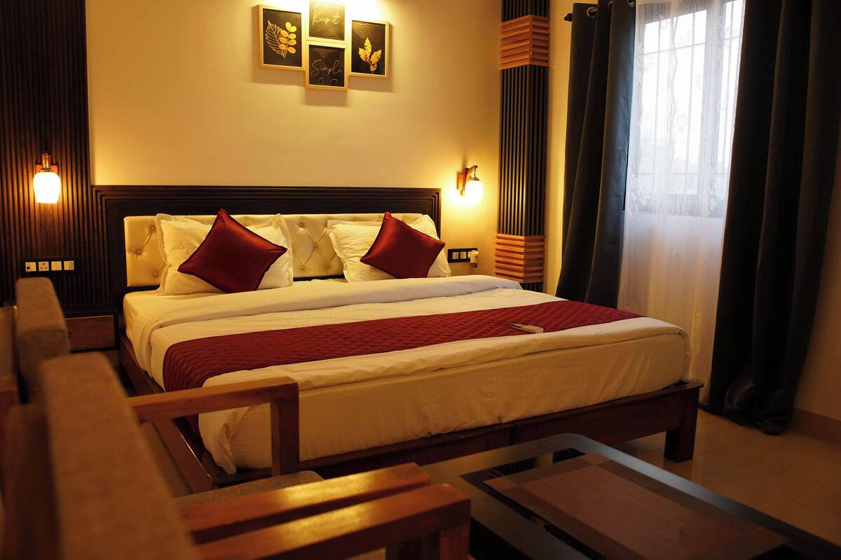 Quarto de hotel com uma cama grande, duas mesas de cabeceira, uma cadeira e uma janela com cortinas.