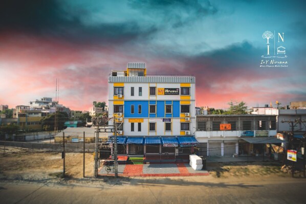A multi-story hotel with a blue and yellow facade, a sign indicating it is a hotel, and a logo for 'Nirvana'. - Ivy Nirvana (Lakhisarai)
