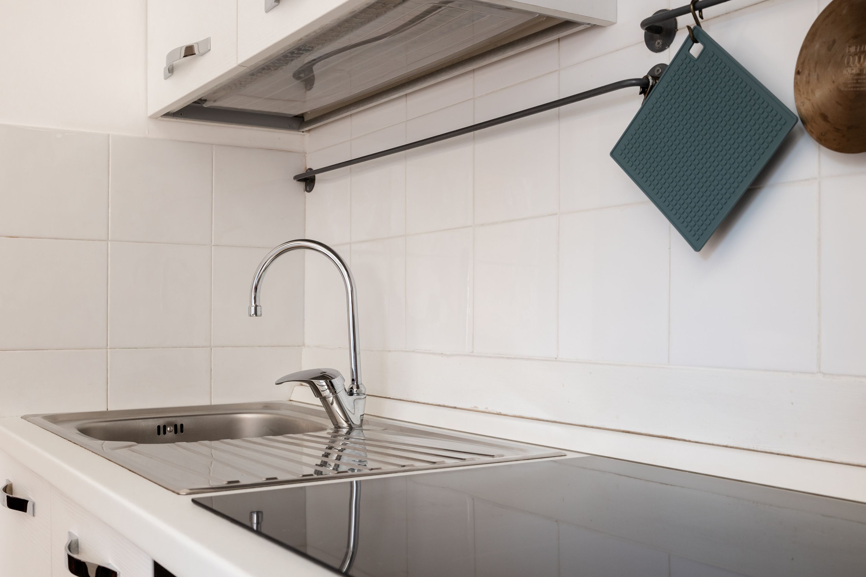 A modern kitchen with a stainless steel sink, a black countertop, and a hanging green towel.