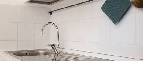 A modern kitchen with a stainless steel sink, a black countertop, and a hanging green towel.