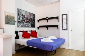 A neatly arranged hotel room with a bed, pillows, a blue bedspread, a cityscape poster, and a mirror with a geometric frame. - Montagnola Mini House (Rome)