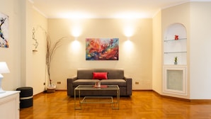 A living room with a grey sofa, a glass coffee table, and a colorful abstract painting on the wall. - Casa Savorelli in Rome (Rome)