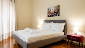 A neatly made bed with white linens, a grey headboard, and a red bedside table with a lamp. - Casa Savorelli in Rome (Rome)