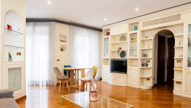 A living room with a wooden floor, a glass coffee table, a sofa, a TV, and a dining area with chairs and a table. - Casa Savorelli in Rome (Rome)