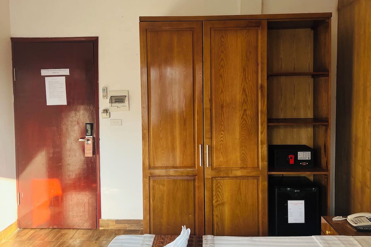 A hotel room with a wooden wardrobe, a desk with a telephone, and a bed with a striped bedspread.