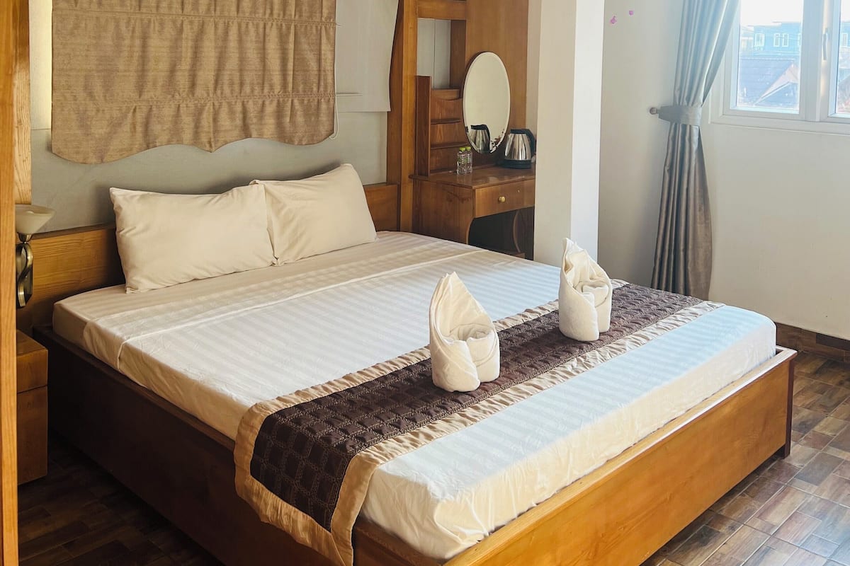 A spacious bedroom with a large bed, wooden headboard, and a bedside table with a mirror.