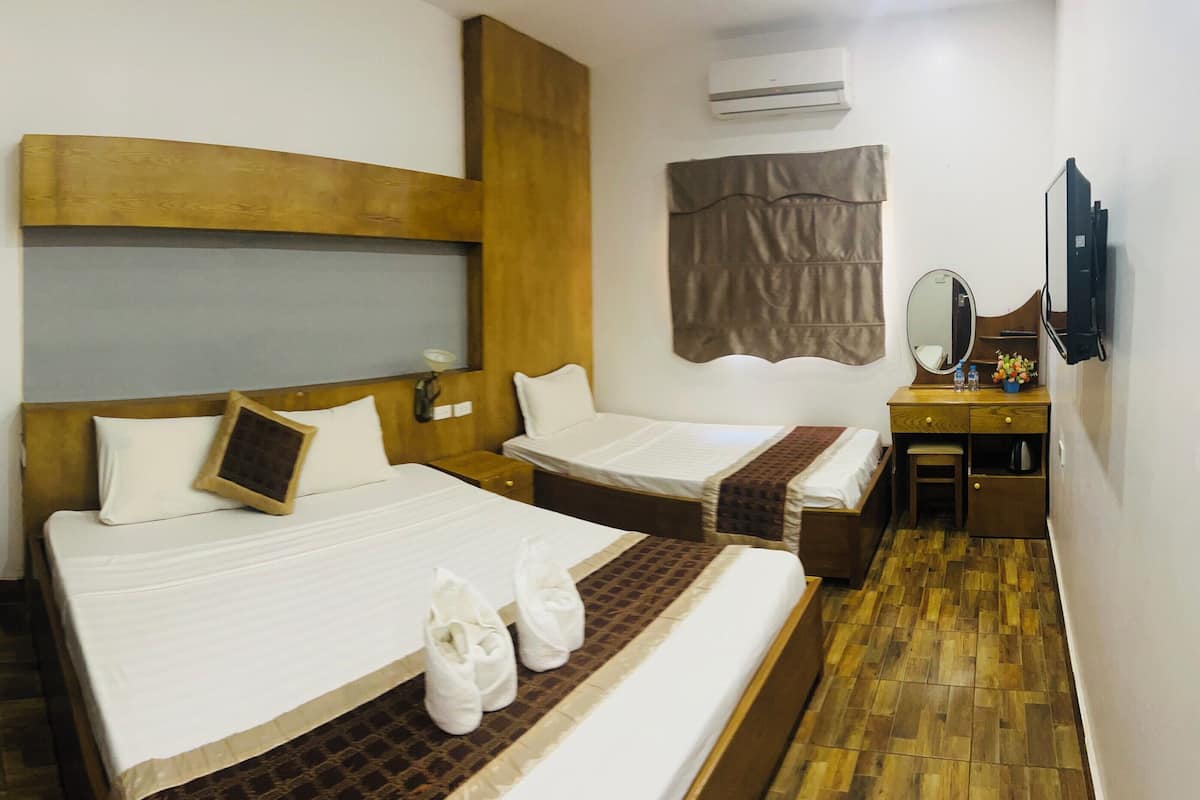 A hotel room with two beds, a wooden headboard, a small desk with a mirror, and a TV.