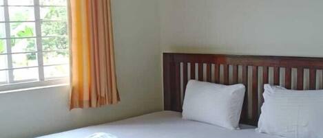 A single bed with a wooden headboard, a ceiling fan, a window with curtains, and a painting on the wall.