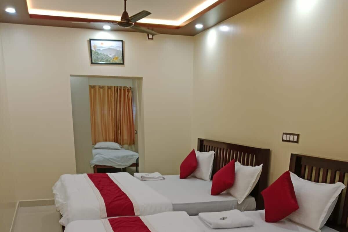 Habitación de hotel con dos camas, cada una con ropa blanca y detalles rojos, un ventilador de techo y un cuadro en la pared.