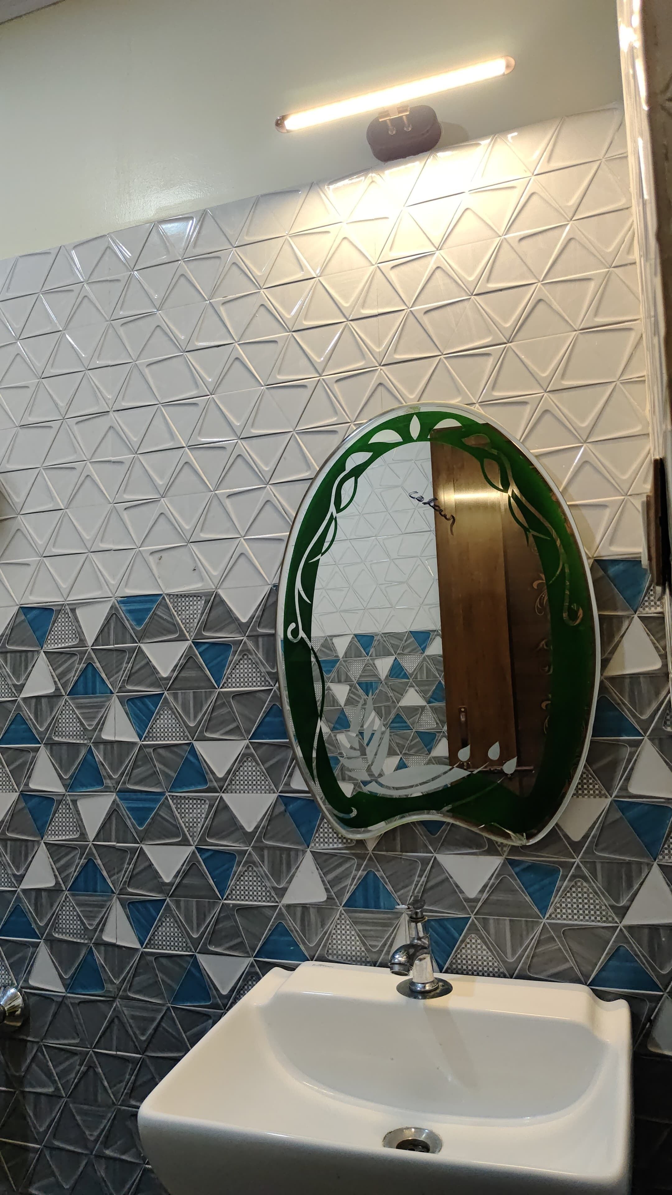 A bathroom with a white sink, a mirror with a green frame, and a patterned tile wall.