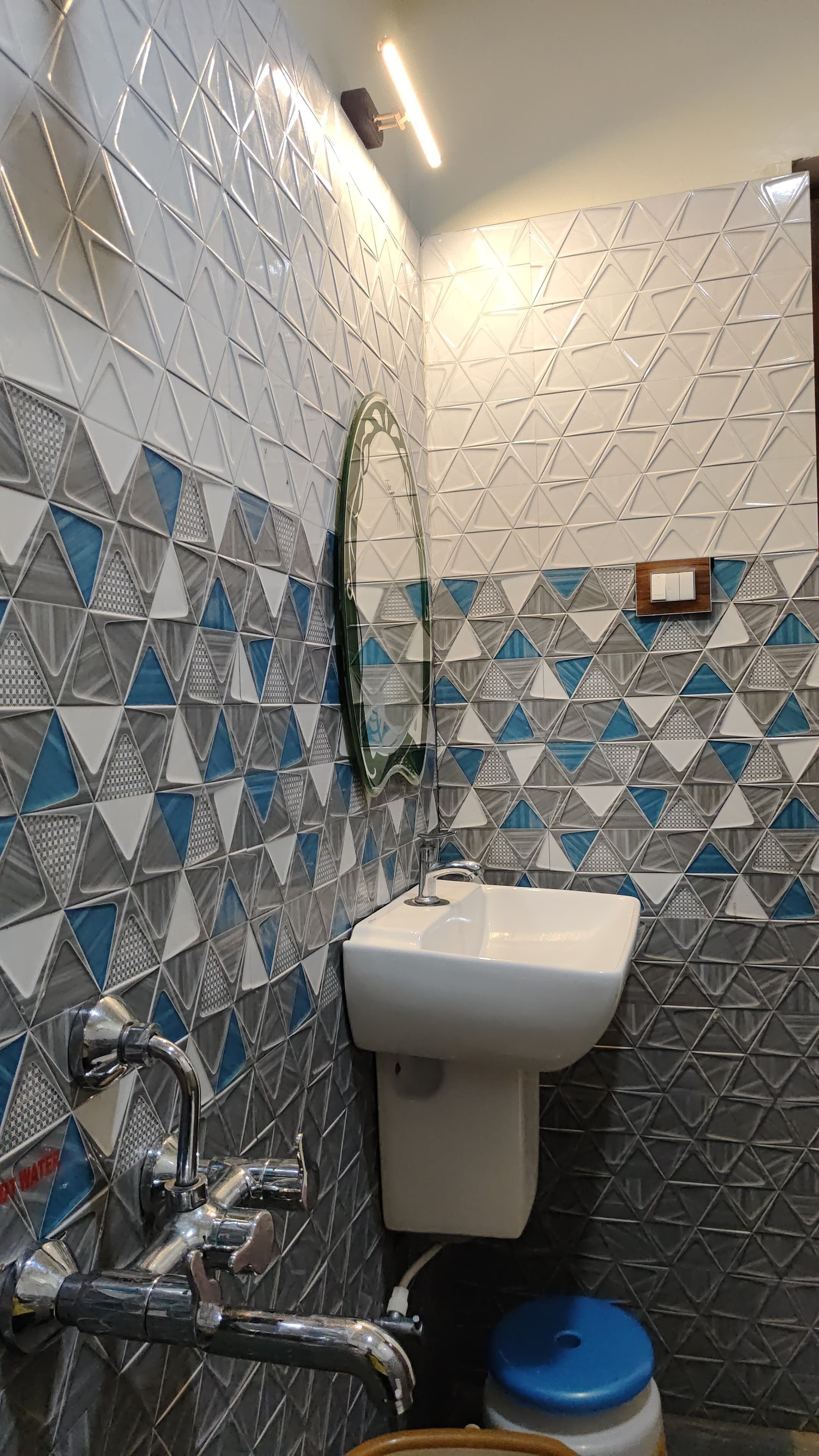 Un baño con lavamanos blanco, un espejo y un inodoro. Las paredes están revestidas con un patrón geométrico.